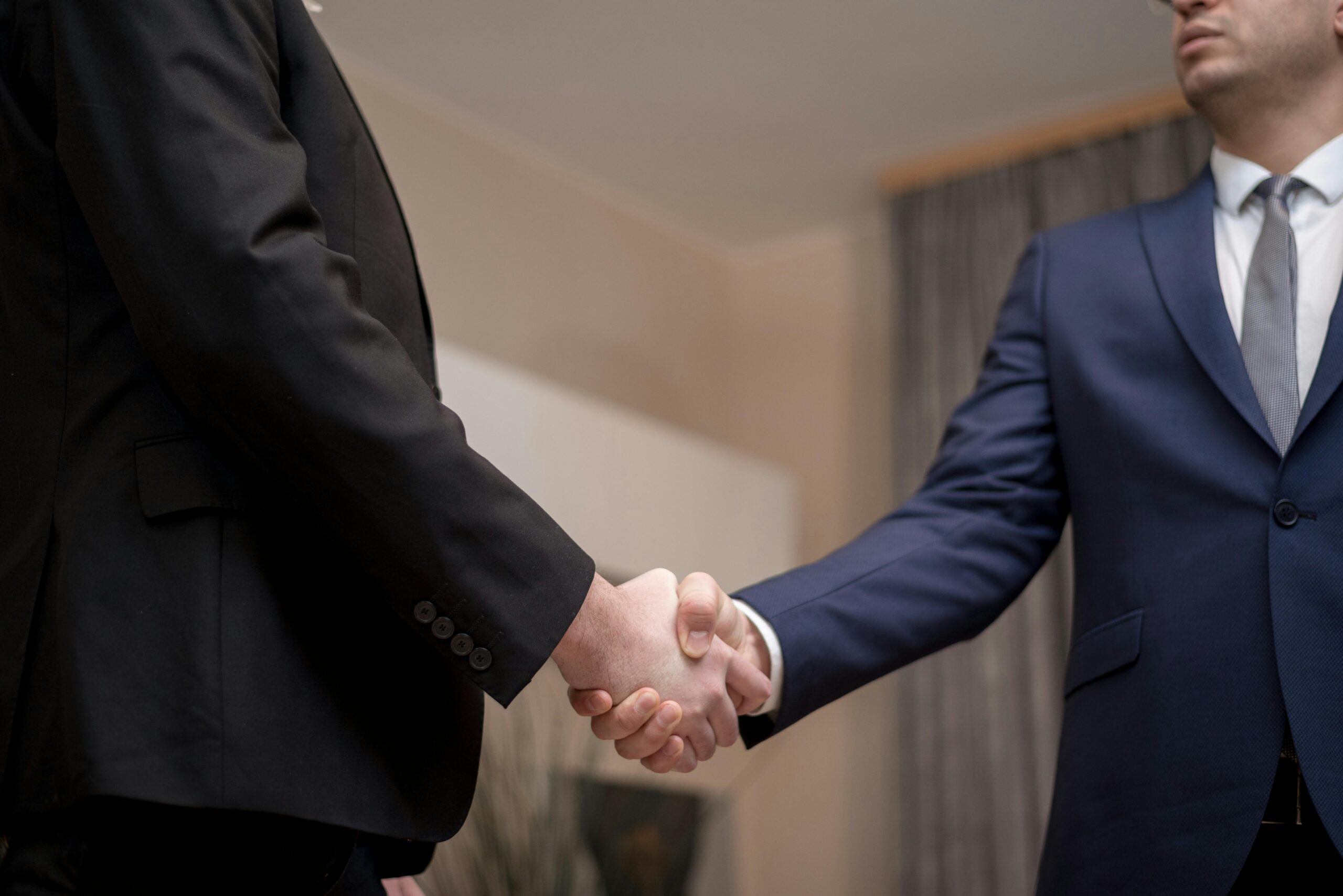 Why OpenAI and ServiceNow’s AI-Agent New Deal Could Quietly Transform Two businessmen in suits shaking hands, emphasizing trust and partnership indoors.