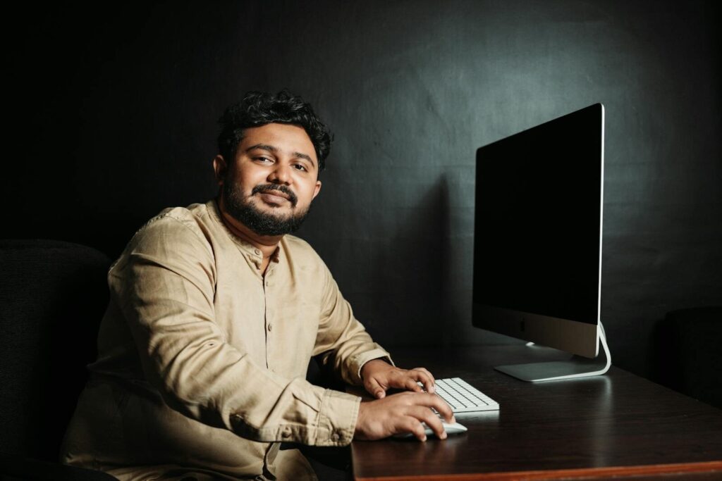 Portrait of a man working at a desk with a computer, in a dimly lit office setting.