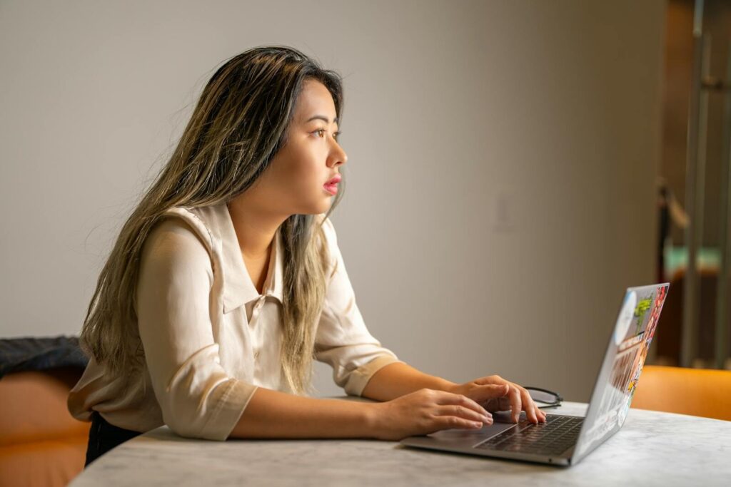 AI Is Supercharging the Internet’s Old Privacy Problems and Creating New Ones Young Asian woman concentrating on work, sitting at a desk using a laptop in an office setting.