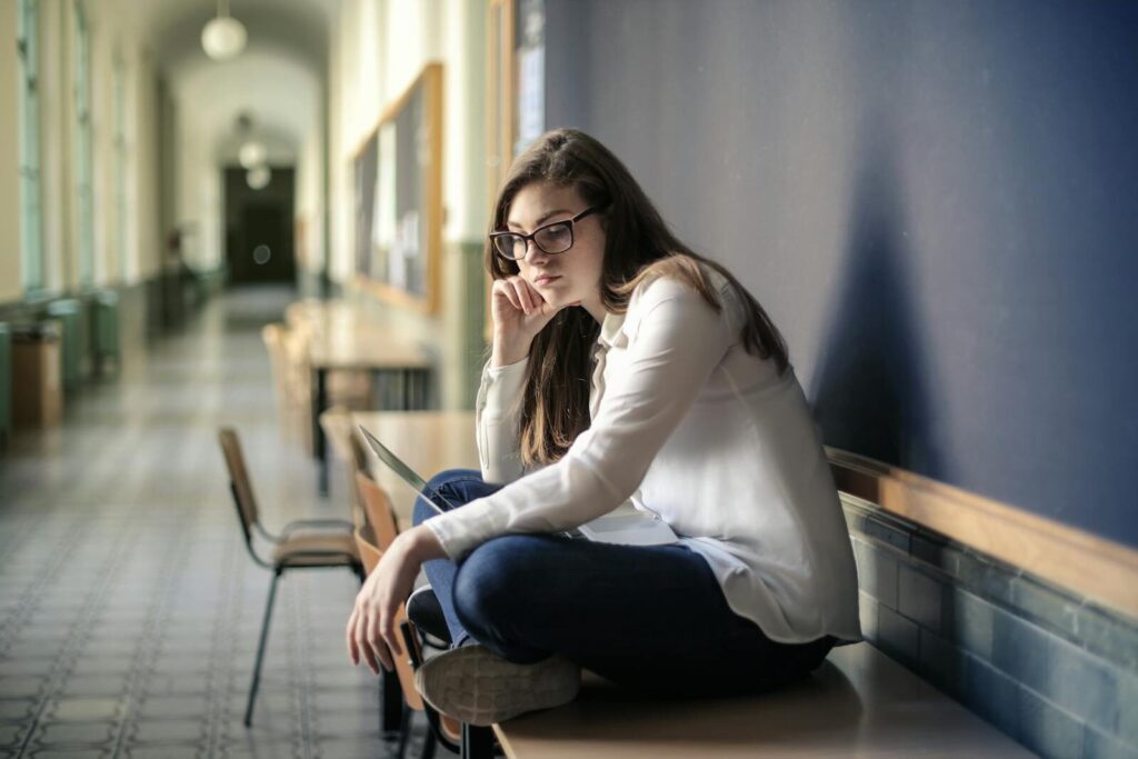 Thoughtful woman sitting alone in a school hallway contemplating problems.