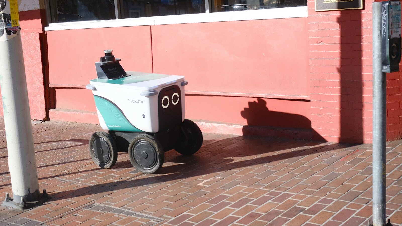 A small delivery robot with a face on the sidewalk.