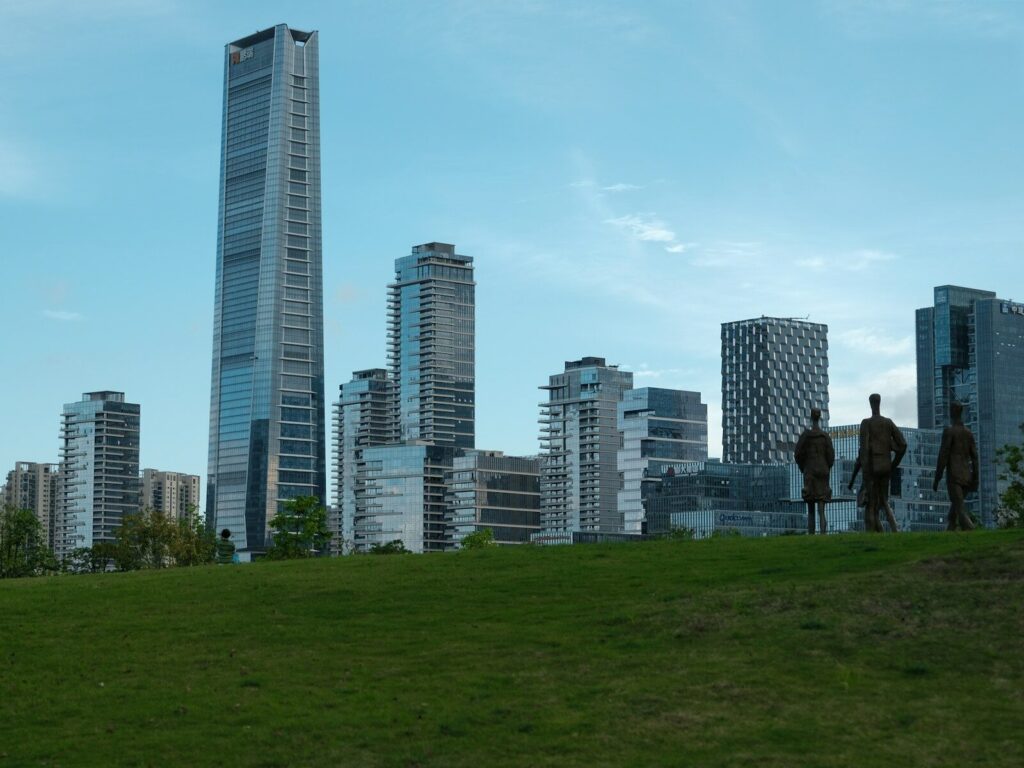 Is AI Really Powering a New Economic Boom or Just Inflating Expectations? Modern skyscrapers rise above a grassy park with statues.