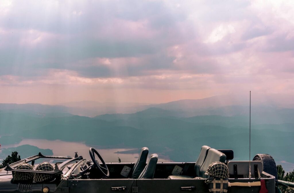 A military jeep parked in a scenic mountain landscape with sunrays piercing through clouds.