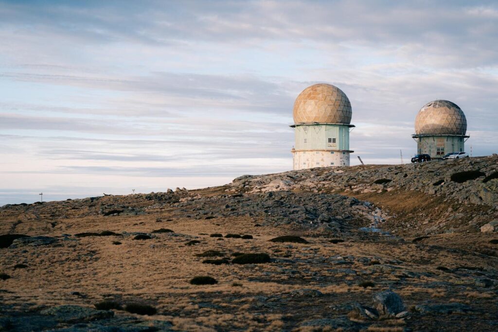 The Pentagon’s New Brain Trust on AI and Space Defense Two radar domes on a rocky landscape under a cloudy twilight sky, symbolizing technology and isolation.