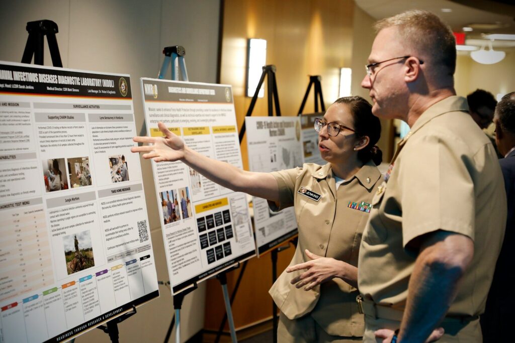 The Pentagon’s New Brain Trust on AI and Space Defense Two people in uniform discuss a presentation board of posters