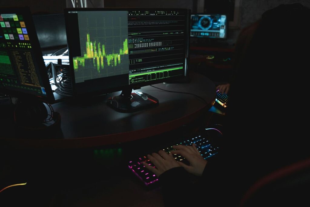 Why Anthropic Is Hiring New Experts to Prevent Dangerous Misuse A cybersecurity expert in a dimly lit room is typing on a colorful keyboard with multiple screens displaying data.