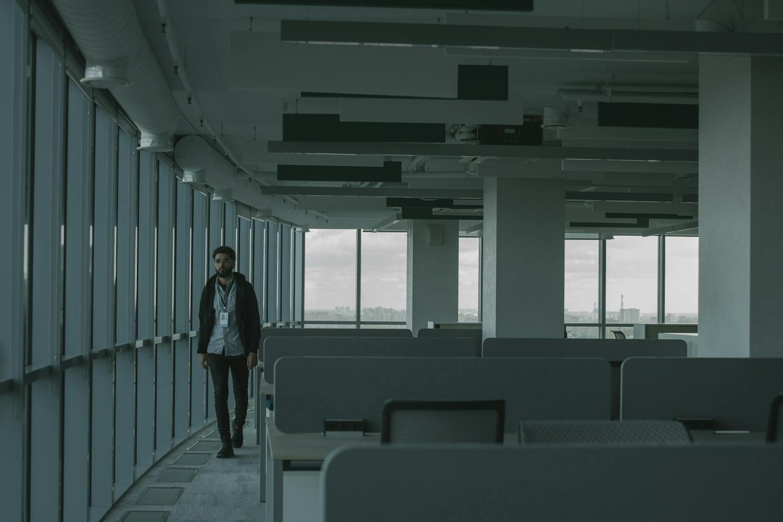 A dimly lit empty office space with one person walking, providing an atmosphere of isolation.