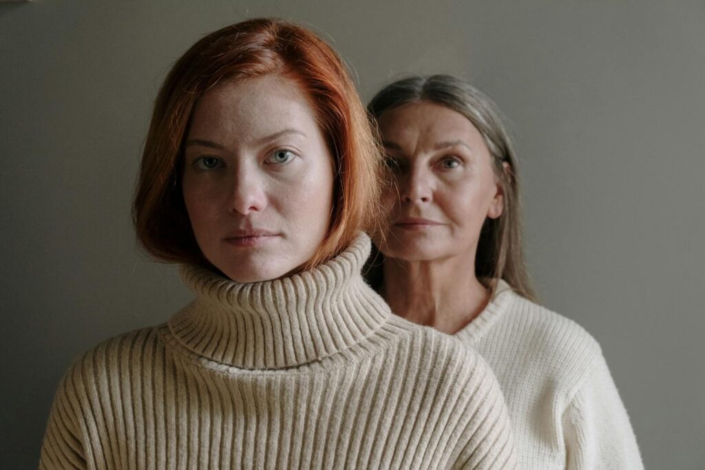 A serene portrait of a mother and daughter in cozy sweaters against a gray background.