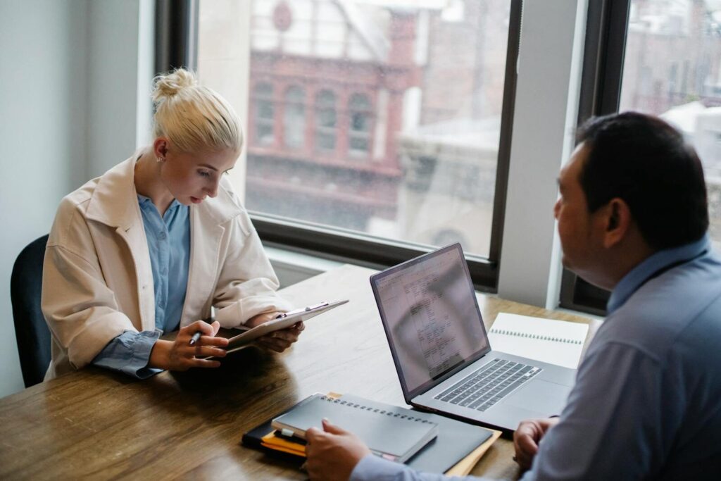Two colleagues in a focused discussion at an office desk with digital devices.