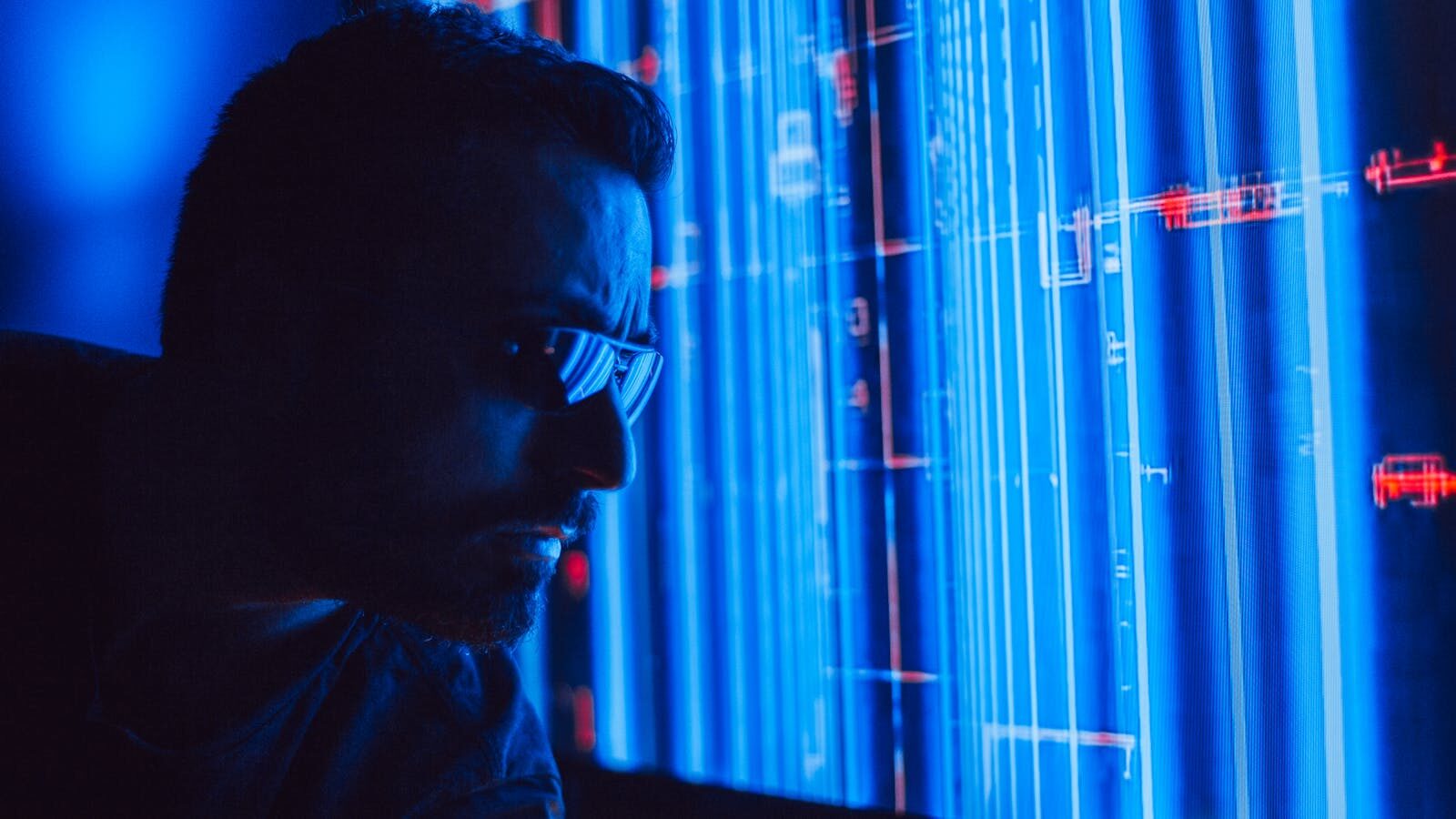 A man in sunglasses intently studies a vibrant blue holographic screen, symbolizing digital technology.