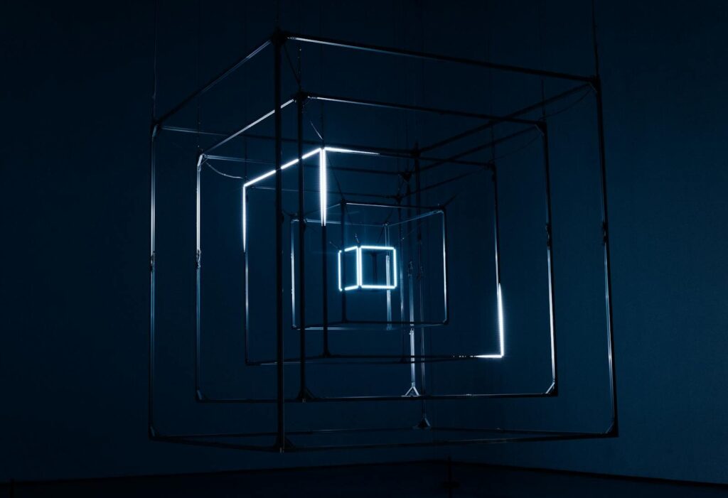 How AI Colliding With New World’s Growing “Polycrisis” A captivating geometric light installation using cubes and neon lights against a dark background.