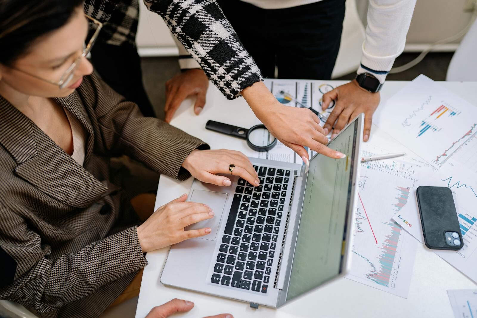 A group of colleagues working together on a laptop amidst documents. Collaborative teamwork in a modern office environment.