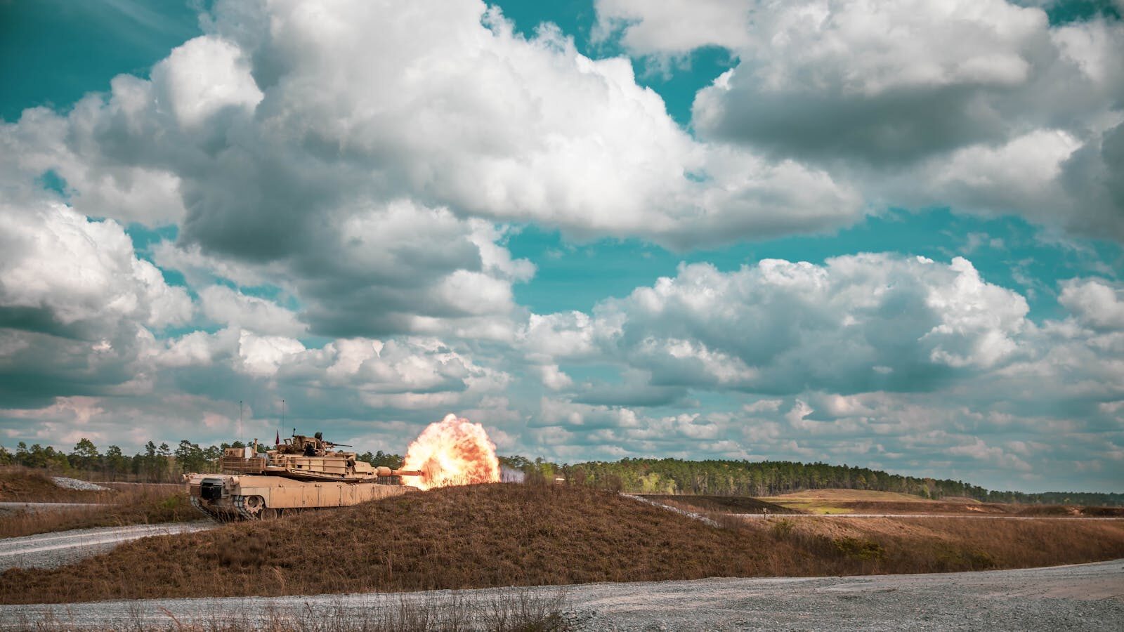 A military tank fires a shot in an open landscape under a dramatic sky.