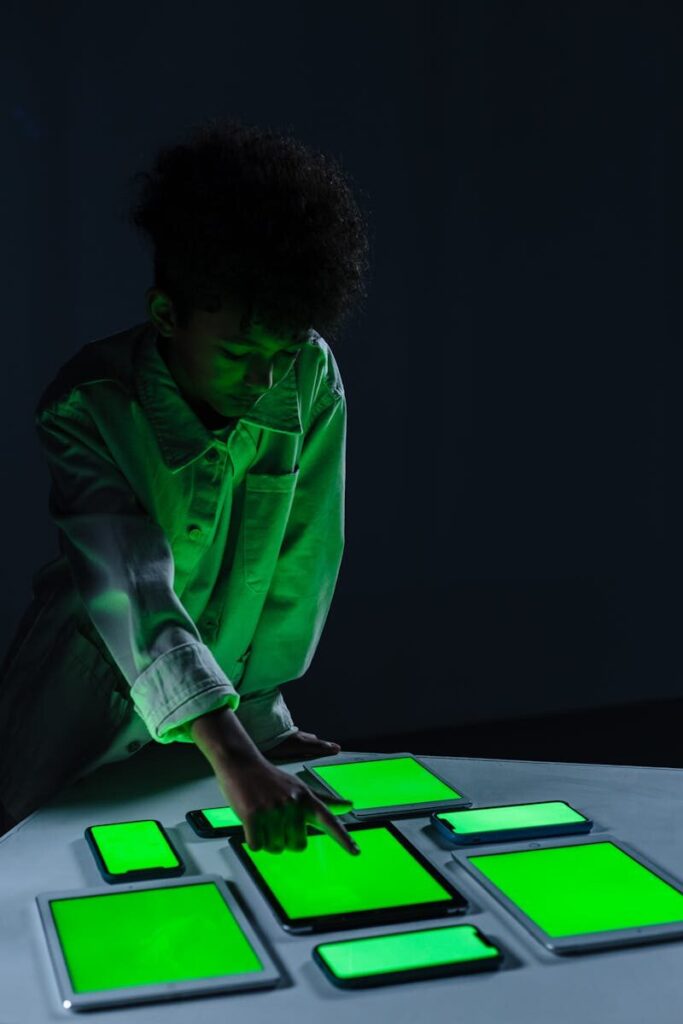 How Rivalries Between Tech Titans Are Defining New Future Intelligence A child in a dark room interacts with several digital screens, glowing green, illustrating modern technology use.