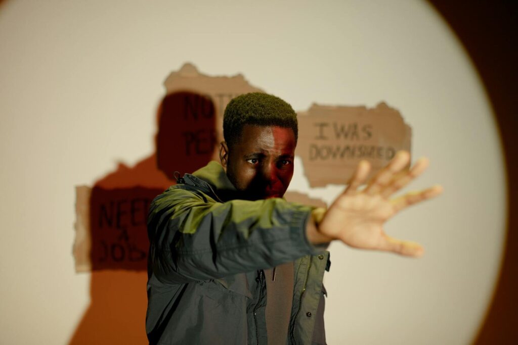 The Next Wave Tech Layoffs Begun And Reshape New Jobs A man stands with an outstretched hand, conveying crisis and unemployment indoors.