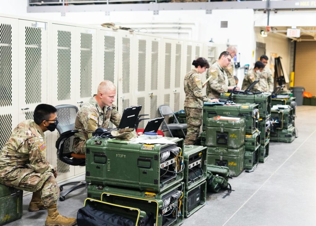 A group of military personnel in uniforms using computers and communication equipment in a secure indoor facility.