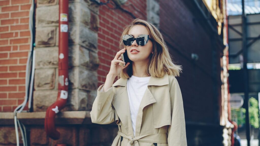 The Endless New Conversation That Won’t Slow Down Woman in trench coat talking on phone outdoors