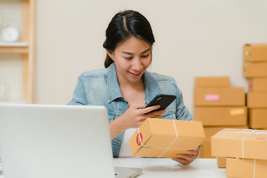 How AI Is Empowering a New Generation of Blue-Collar Entrepreneurs Woman checking package with phone near laptop and boxes