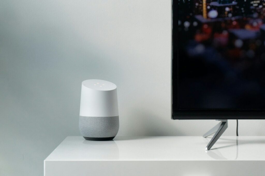 white and gray Google smart speaker beside black flat screen TV