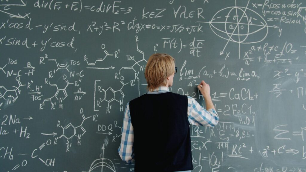 Teacher writing math equations on a chalkboard.