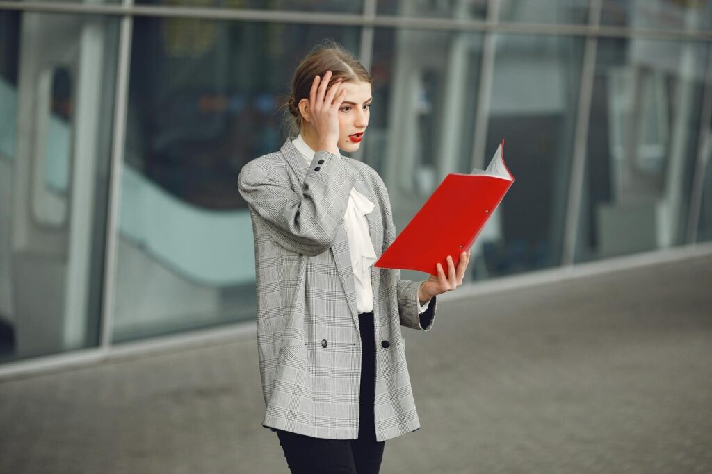 Big Tech Promised New Gradual Shift But Workforce Disruption Faster Woman in business attire looking stressed while holding and reading documents outside.