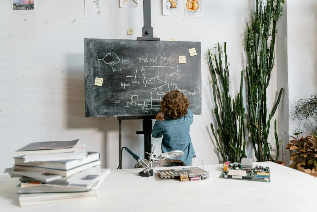 If New AI Can Do Your Homework, Schoolwork Even Necessary? Curious young boy drawing STEM concepts on a blackboard indoors, surrounded by educational materials.