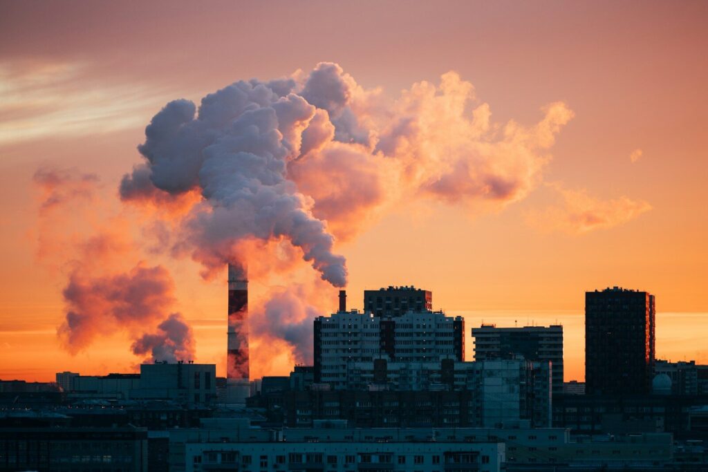 The Explosive Boom Reshaping Economies and New Future of Industry Factory smokestacks emitting smoke against sunset sky.