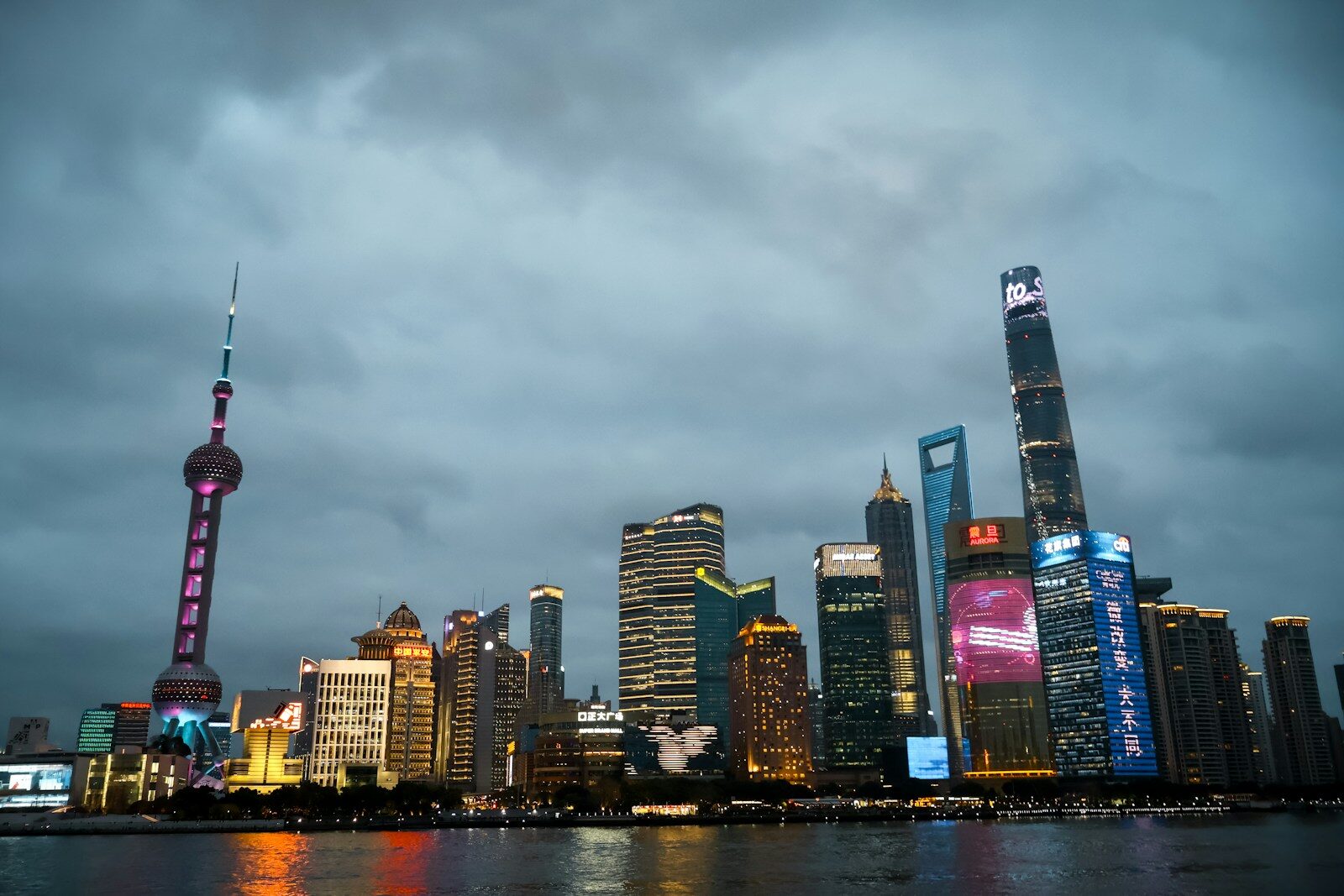 Modern cityscape with illuminated skyscrapers under a cloudy sky.