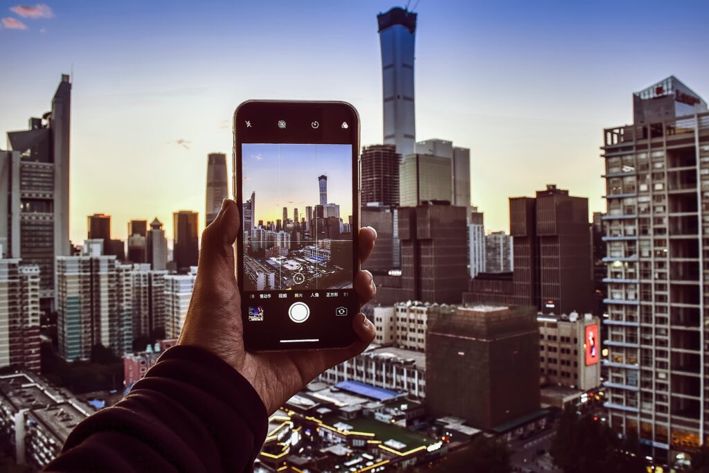 A hand holding a smartphone capturing the stunning Beijing skyline during sunset.