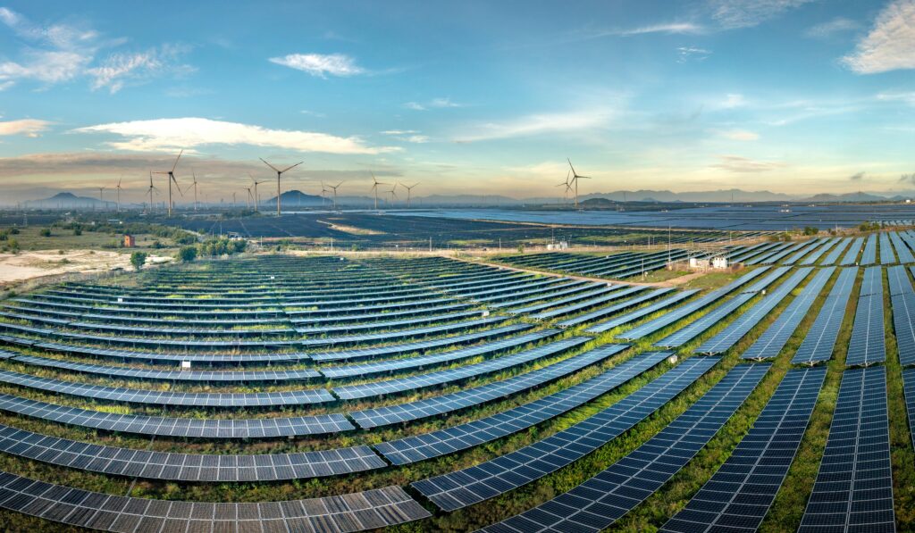 Google DeepMind’s “AI for the Planet” Accelerator Signals New Era Expansive solar farm with wind turbines in the background under a clear blue sky.