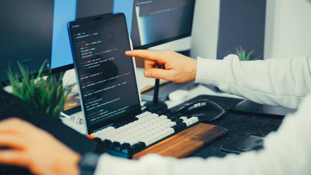 The Hidden Rules That Quietly Control New AI Behavior A programmer working on code with a laptop and monitor setup in an office.