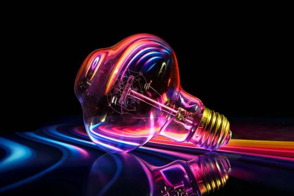 A glowing lightbulb with colorful reflections on a dark background