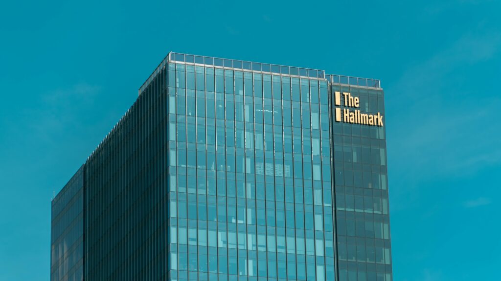 What It Reveals About New True Cost of AI Revolution A tall glass skyscraper named 'The Hallmark' stands out against a clear blue sky.