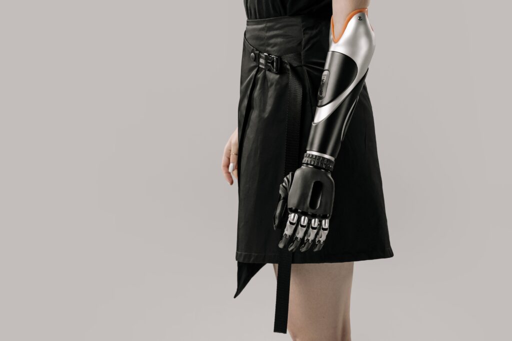 Close-up of a woman wearing a modern prosthetic arm with a stylish black skirt, set against a gray background.
